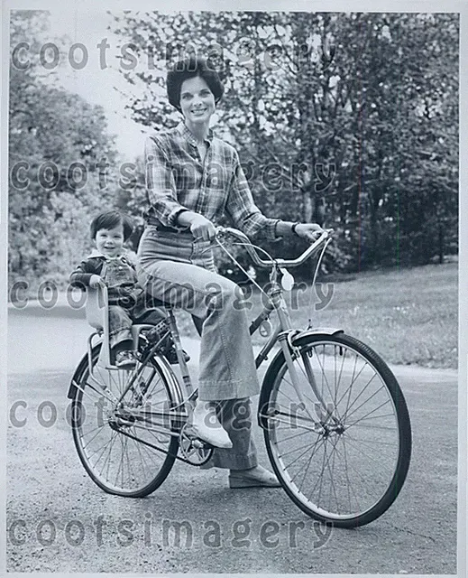 Pretty Woman Riding Bicycle With Child in Toddler Seat Press Photo